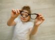 Child girl holding black-framed glasses in hands. Glasses in focus, child is blurred