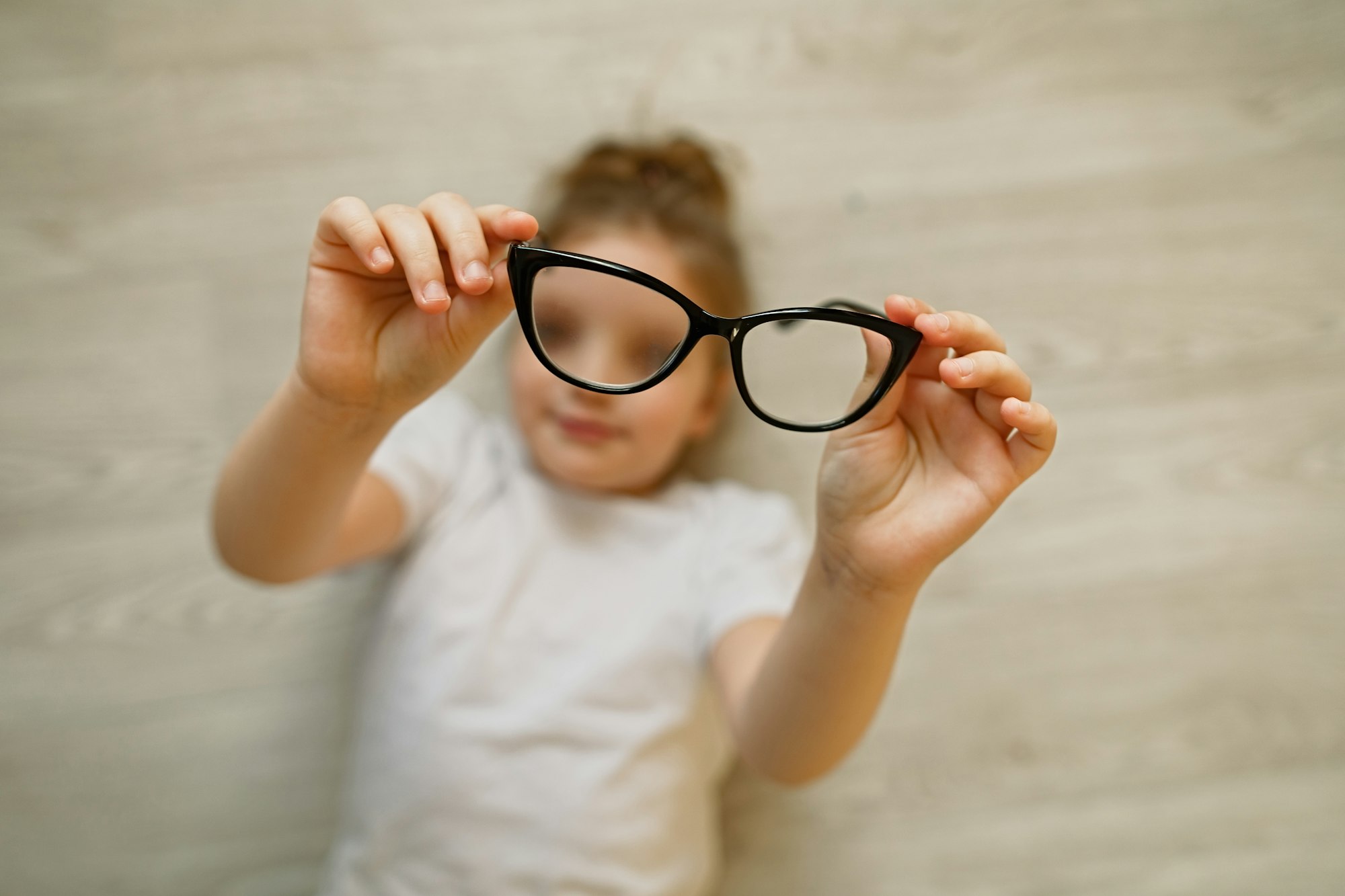 Child girl holding black-framed glasses in hands. Glasses in focus, child is blurred