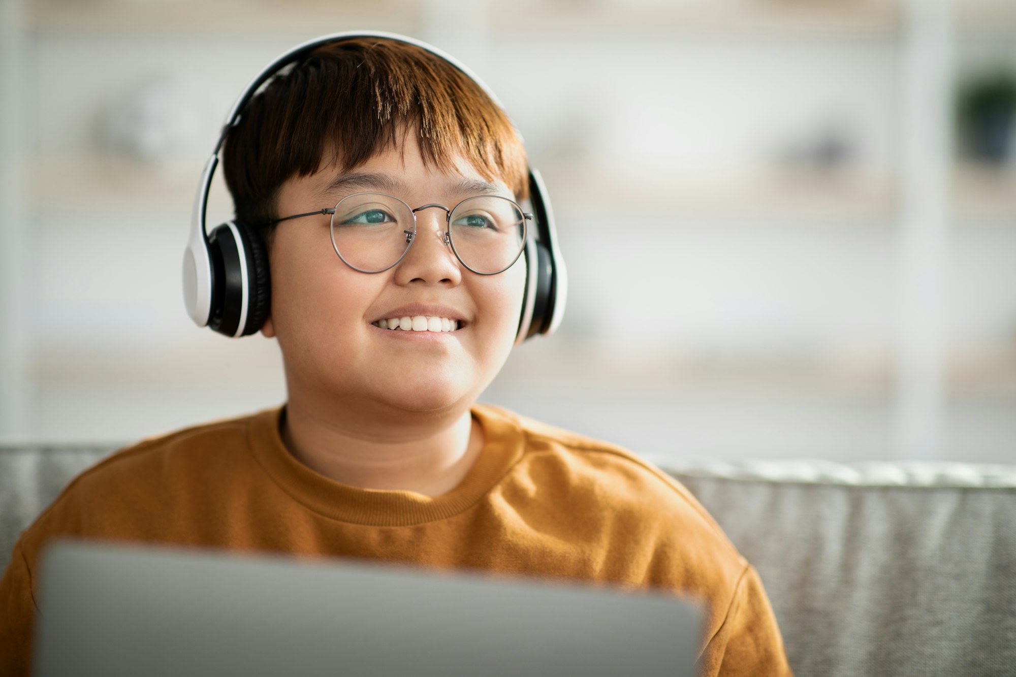 Closeup of cheerful asian kid with wireless headset using laptop